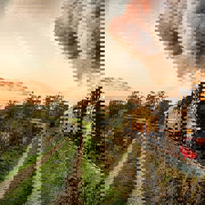 Stoomtrein naast veldweg met ondergaande zon