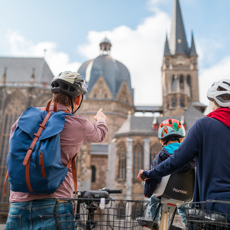 Een fietsend gezin wijst naar de Dom van Aken