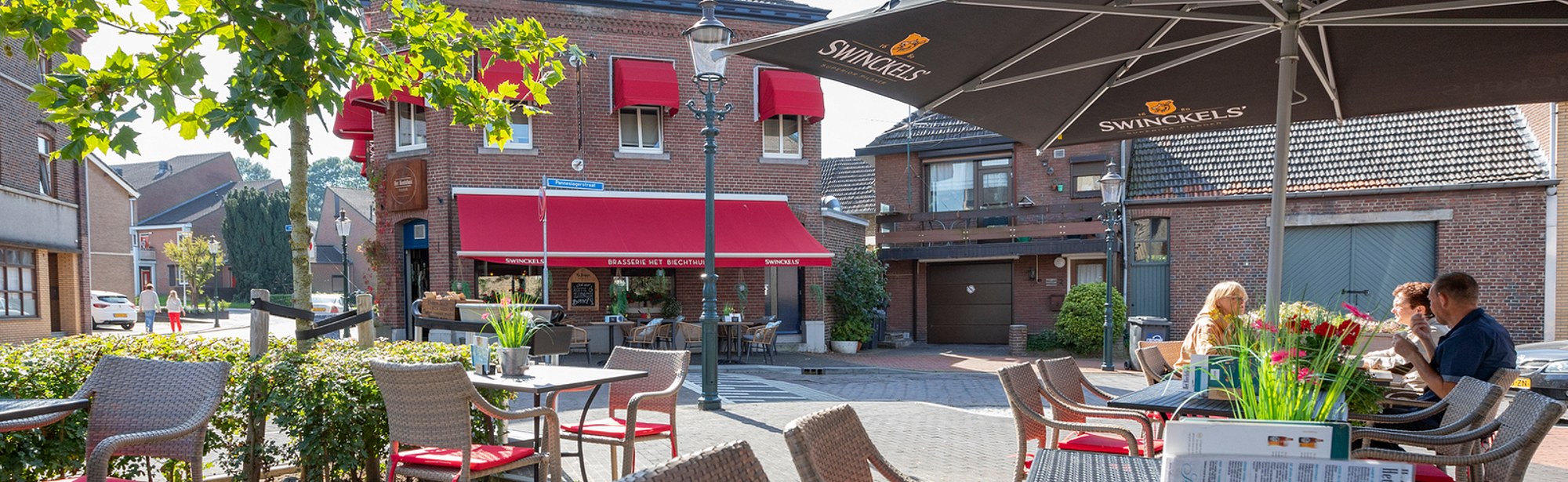 Terras op een klein dorpslein met rode accenten in de kussentjes en luifels voor de ramen. 