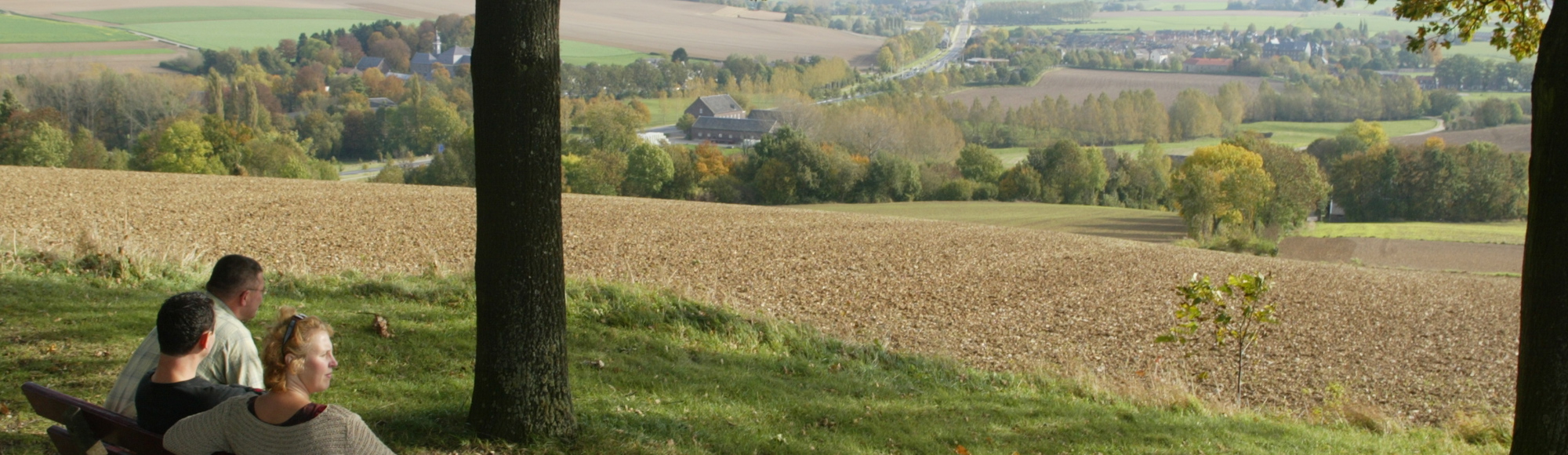 Wandelaars genieten op een bankje waarbij ze uitzicht hebben over Simpelveld. 